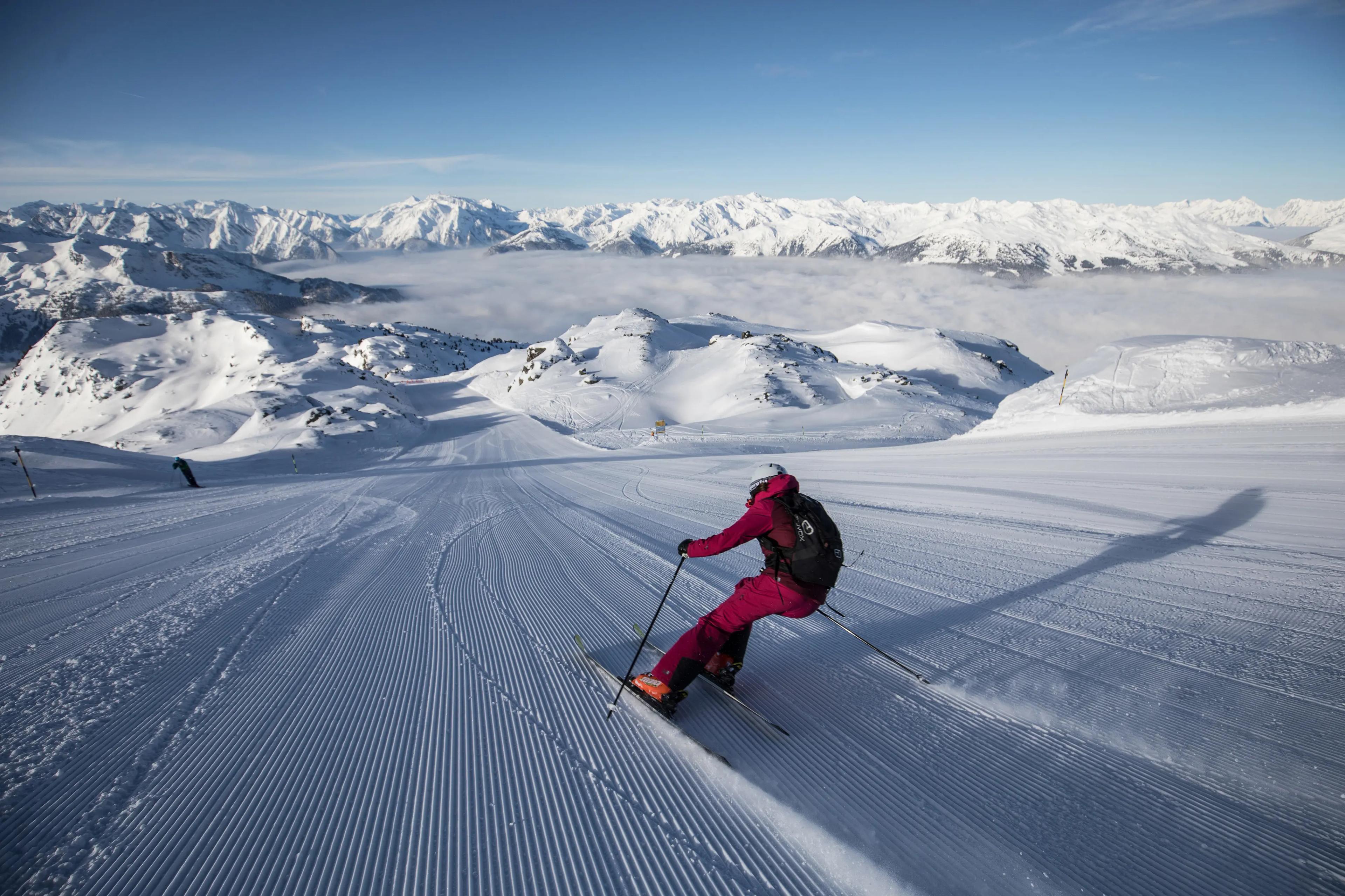 Skidåkare åker nerför en pistad backe i Zell am Ziller, med fantastisk utsikt över Alperna och omgivande berg.